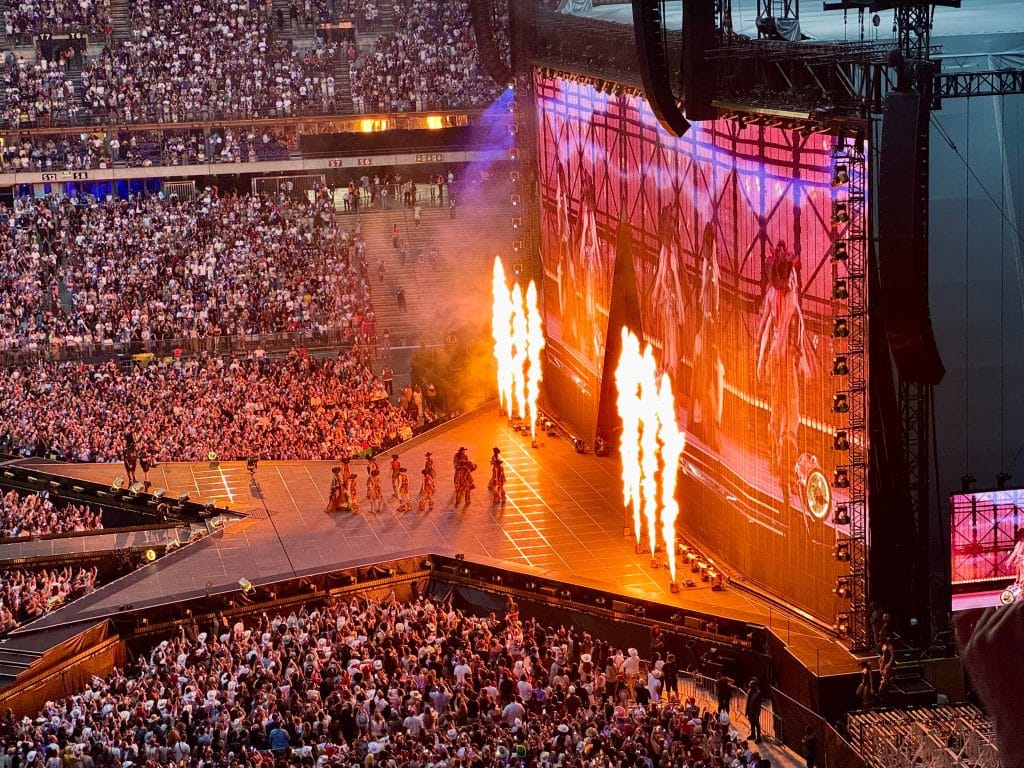 A star-shaped concert stage in Paris, with dancers on it and plumes of fire shooting out from the back.