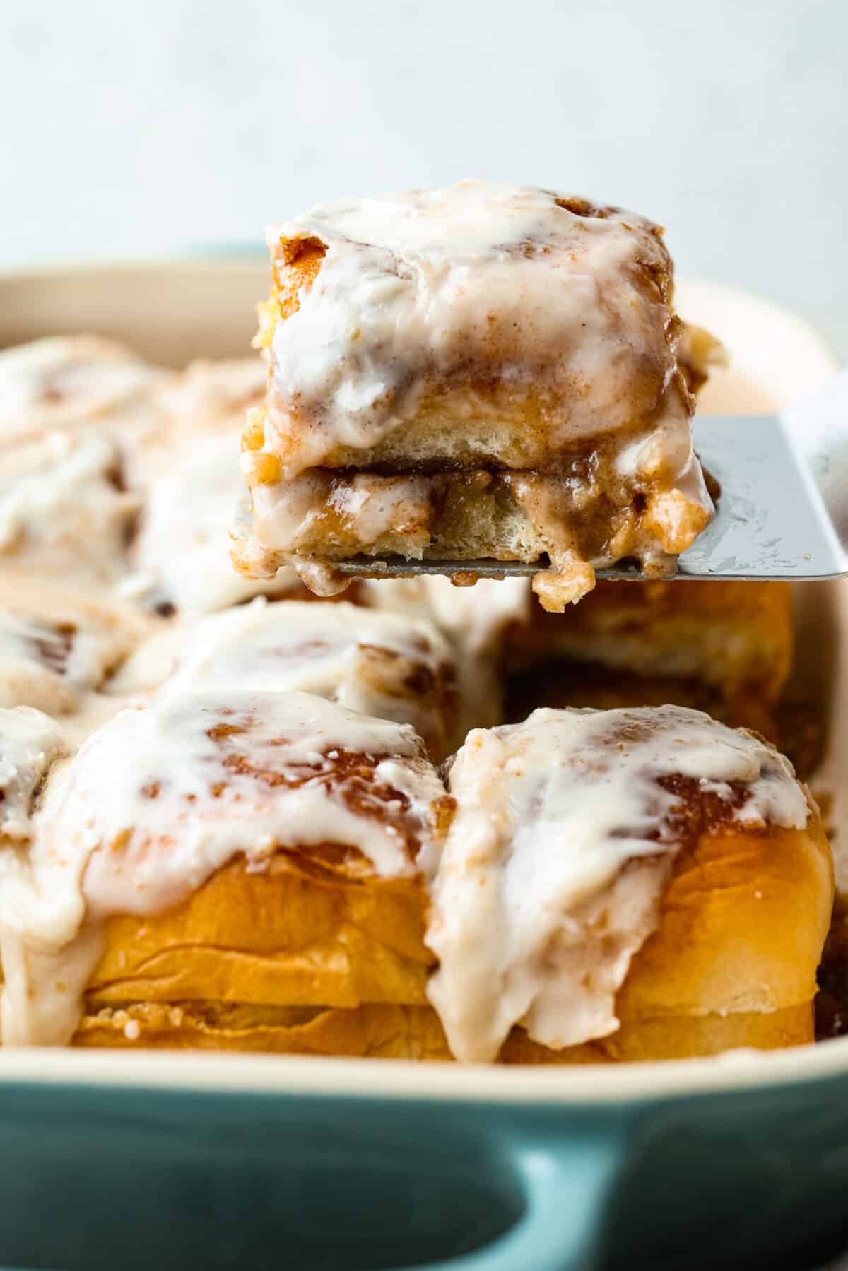 Someone lifting a Hawaiian roll cinnamon roll out of the pan.