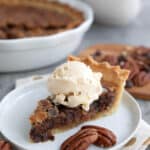 A slice of gooey keto Kentucky chocolate chip pie on a white plate with a scoop of ice cream on top.