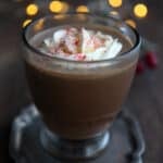 A sugar-free Keto Peppermint Mocha in a glass mug on a dark wooden table, with christmas lights in the background.