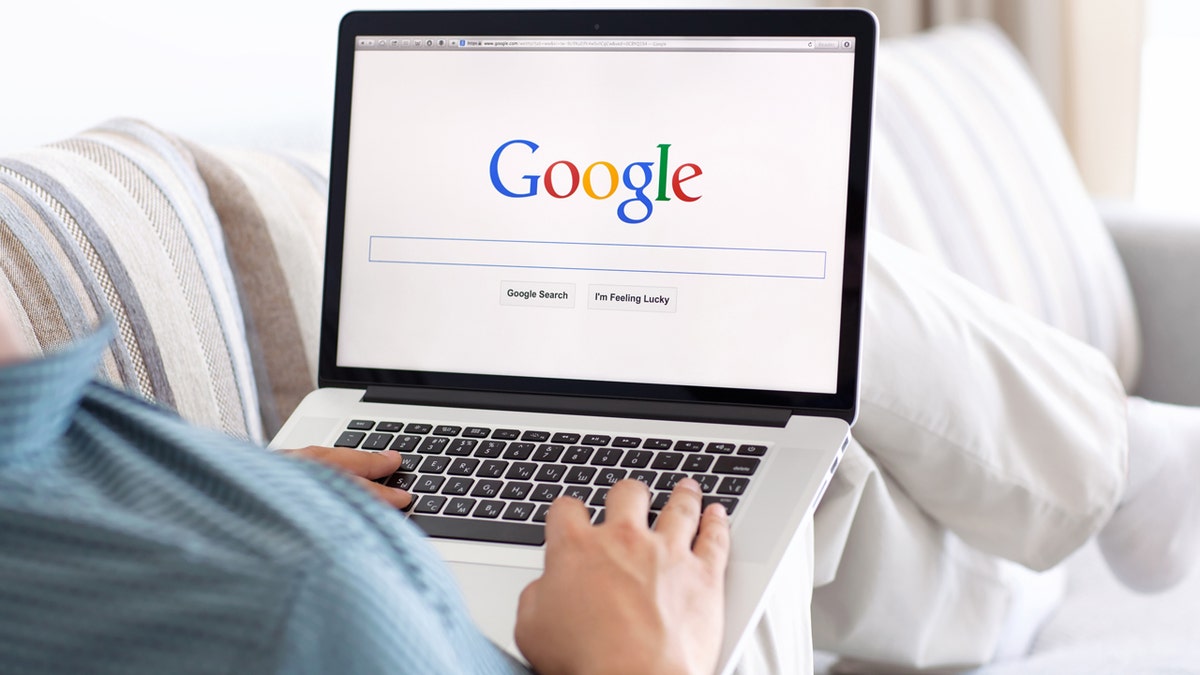 Man sitting with a MacBook on his lap with the Google search engine on the screen