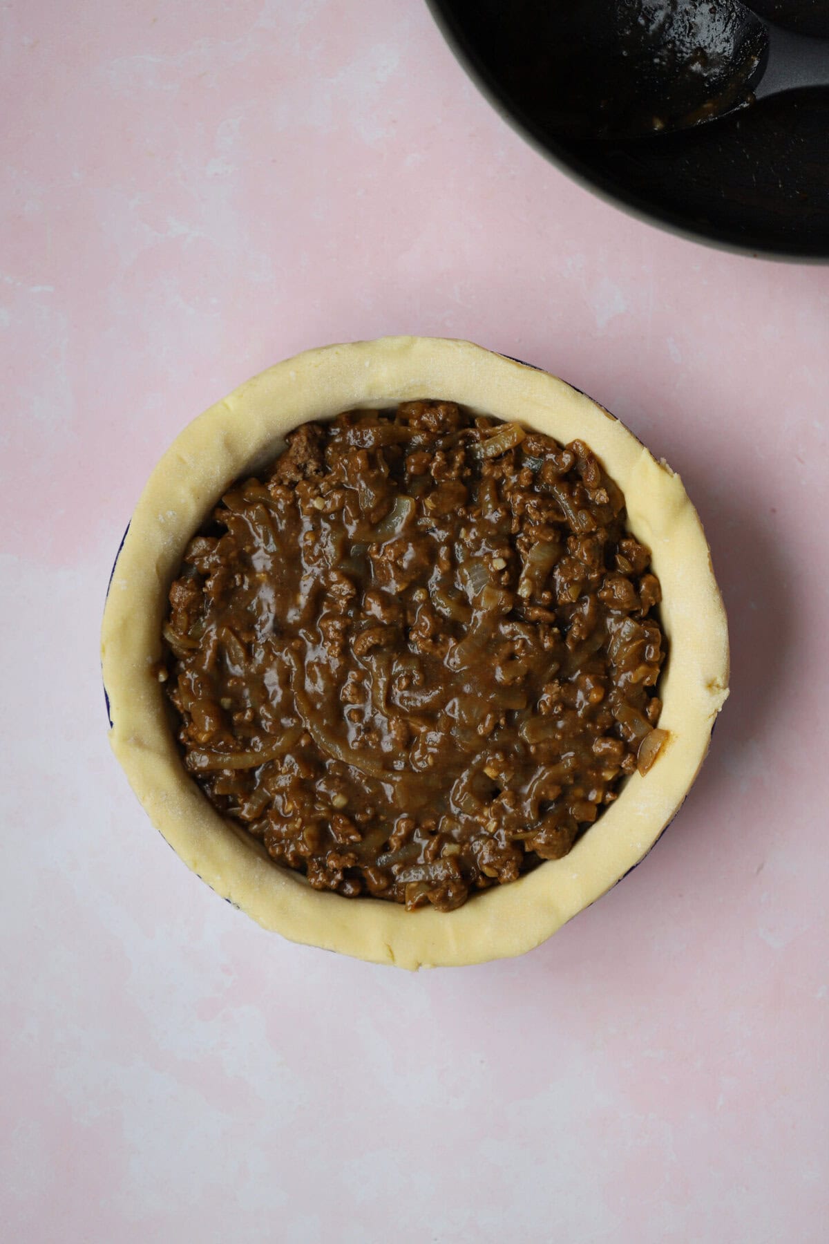 Process shot of a minced beef pie showing the beef filling in the pie, ready to be topped.