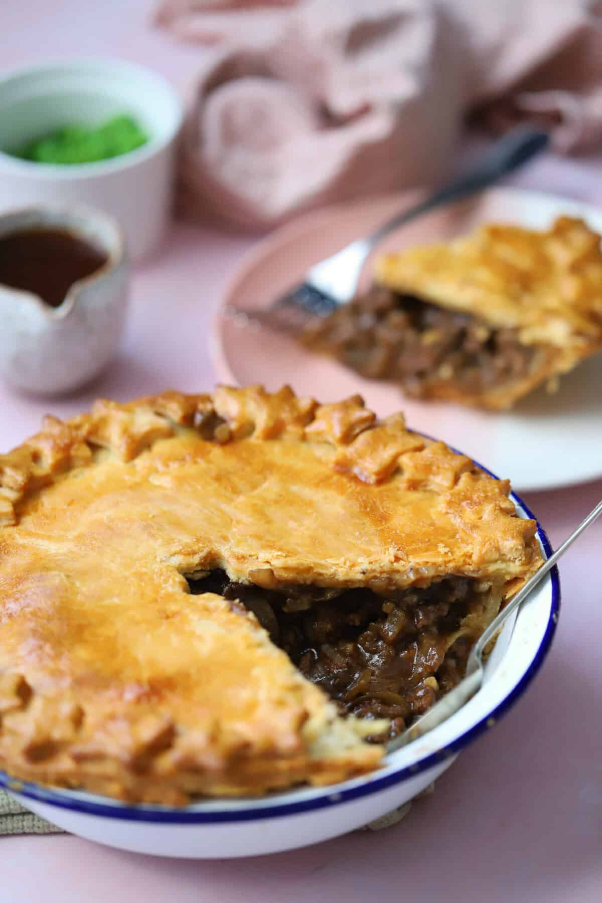 A gluten free minced beef and onion pie with a slice removed, which sits on a plate in the background.