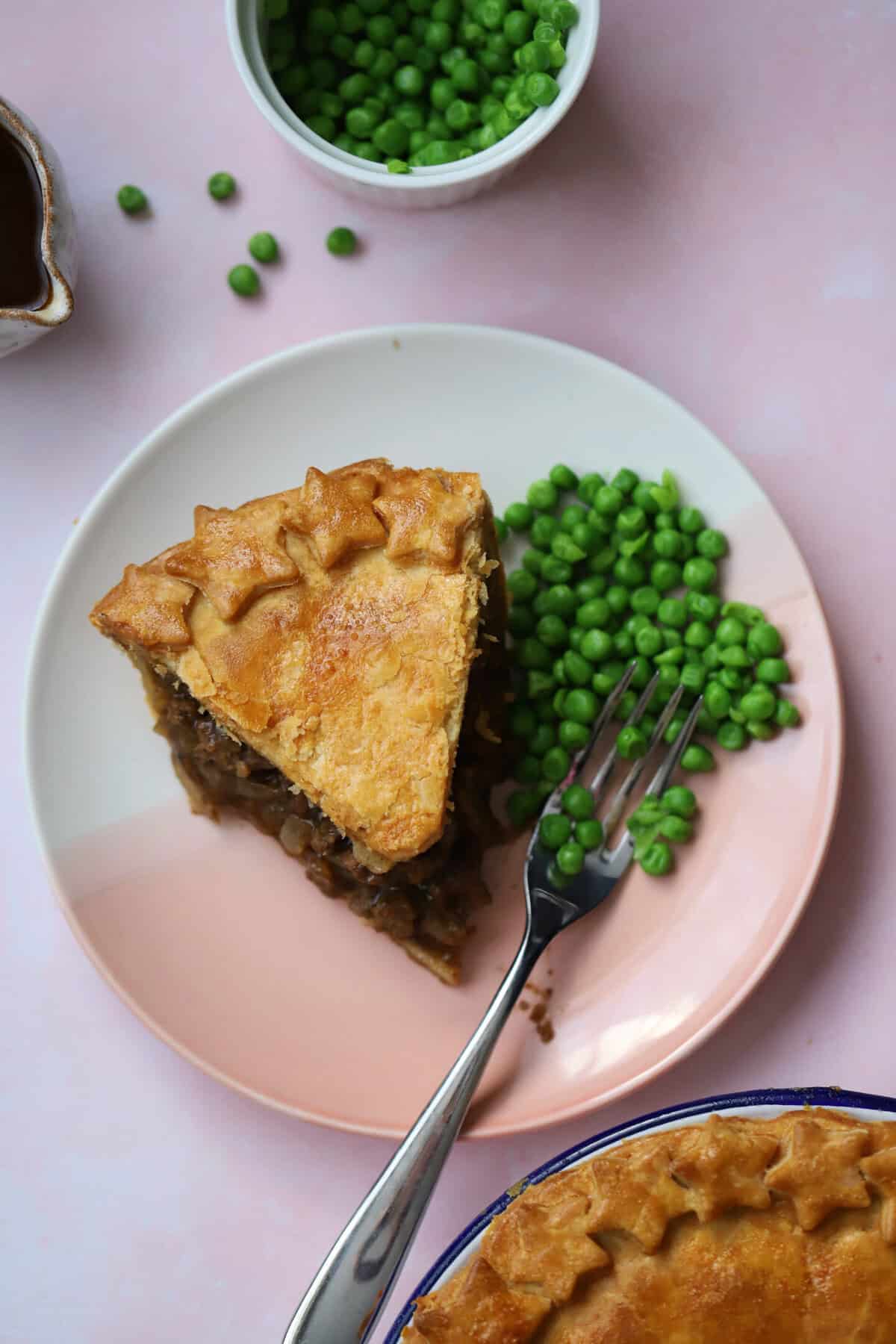 Overhead shot of a slice of minced beef pie on a plate with peas.
