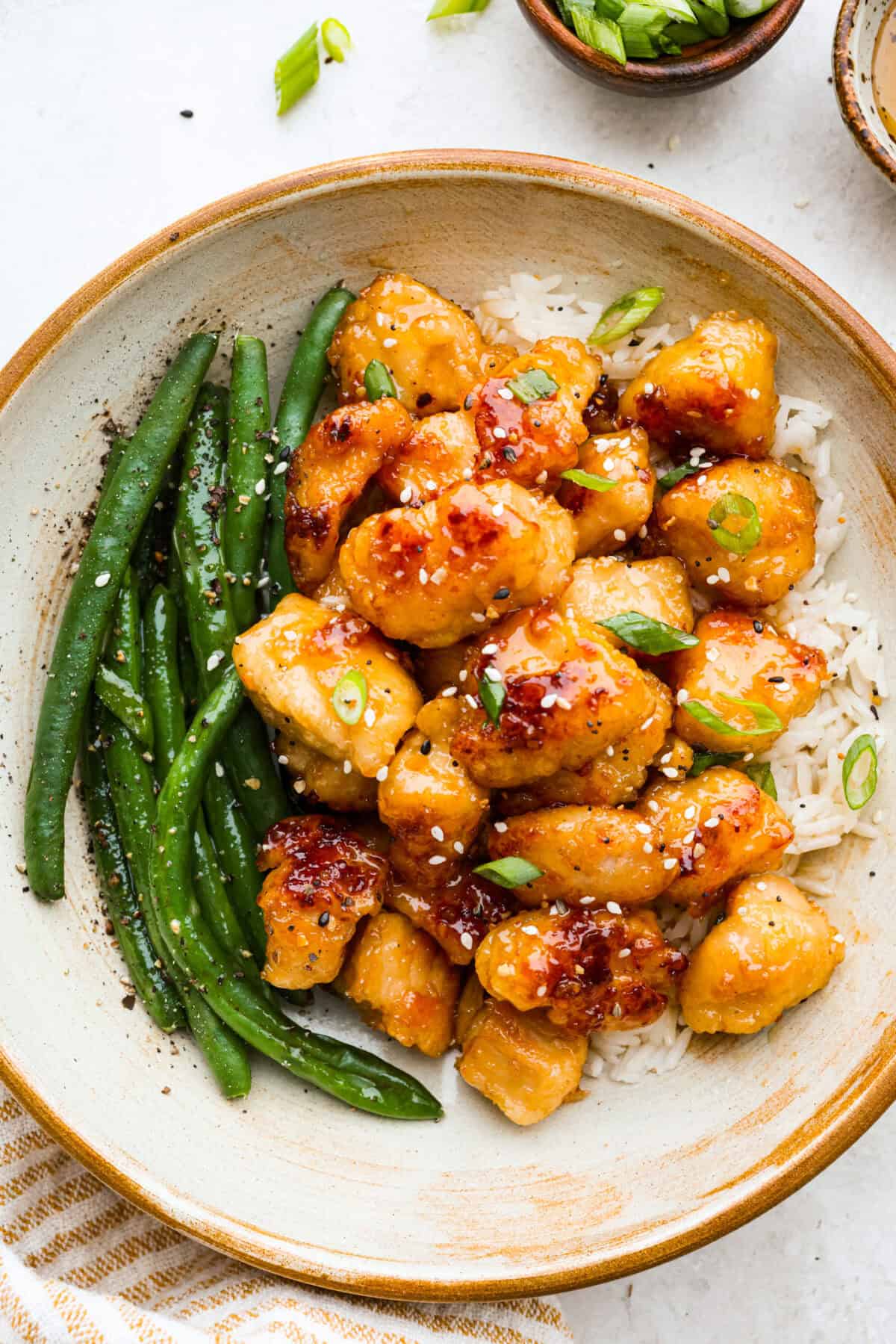 Plated honey butter chicken over rice next to green beans. 
