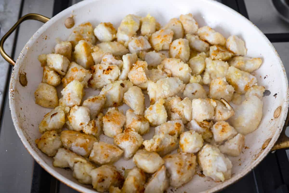Cornstarch covered chicken cooking in a skillet. 