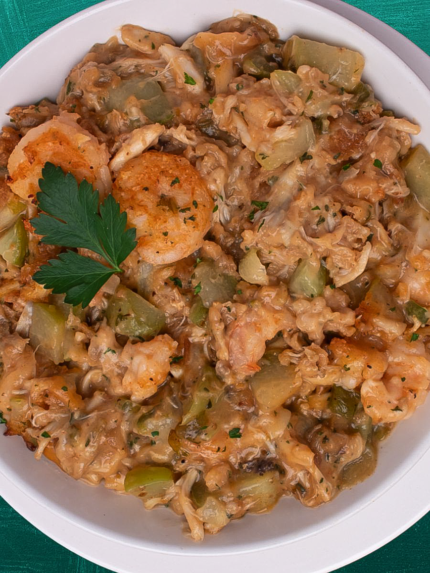 One serving of mirliton dressing in a round white bowl with a green background. 