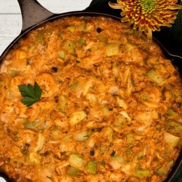 Mirliton dressing in a black cast iron skillet alongside a green napkin and a large mum flower.