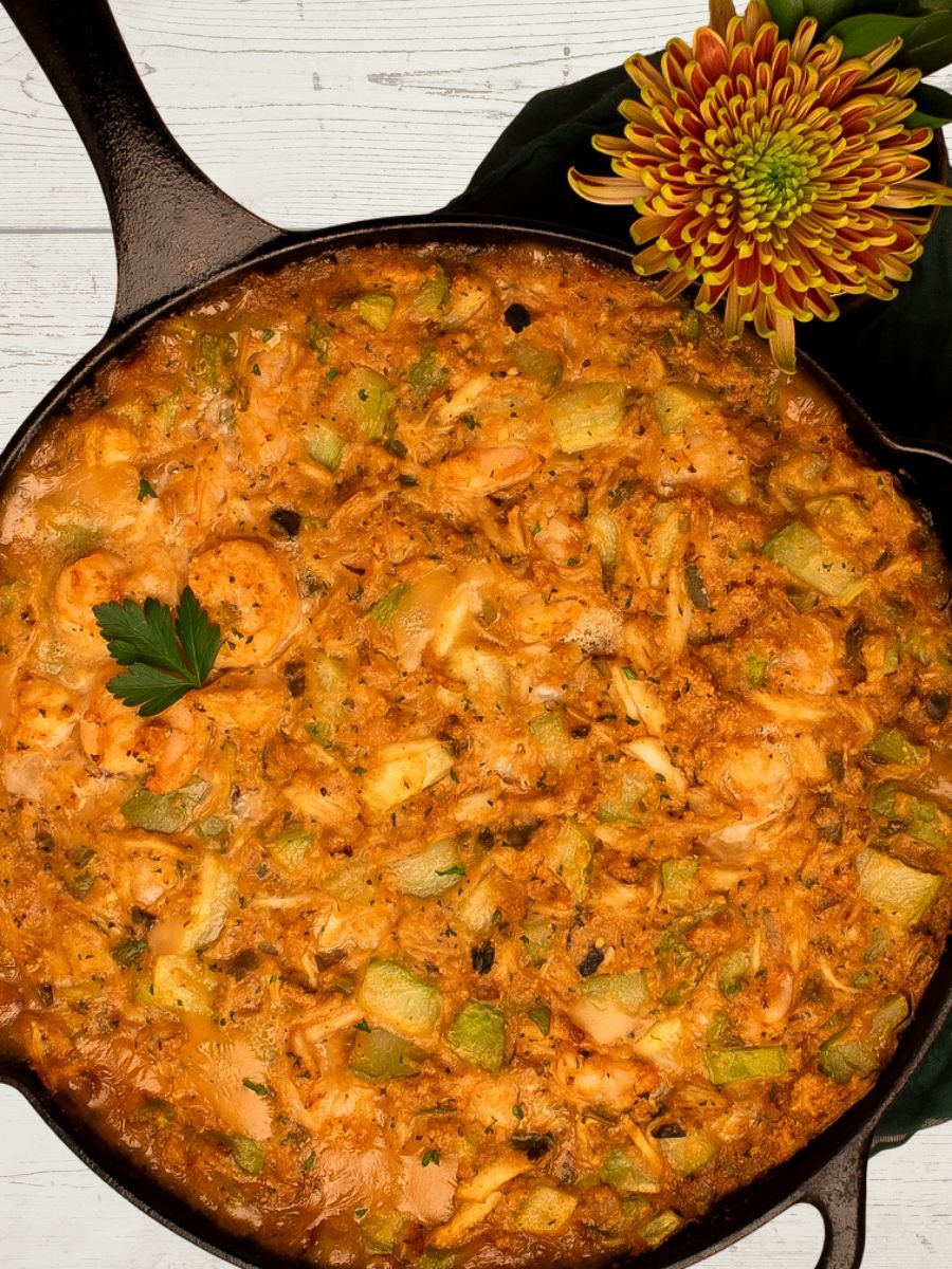Mirliton dressing in a black cast iron skillet alongside a green napkin and a large mum flower. 
