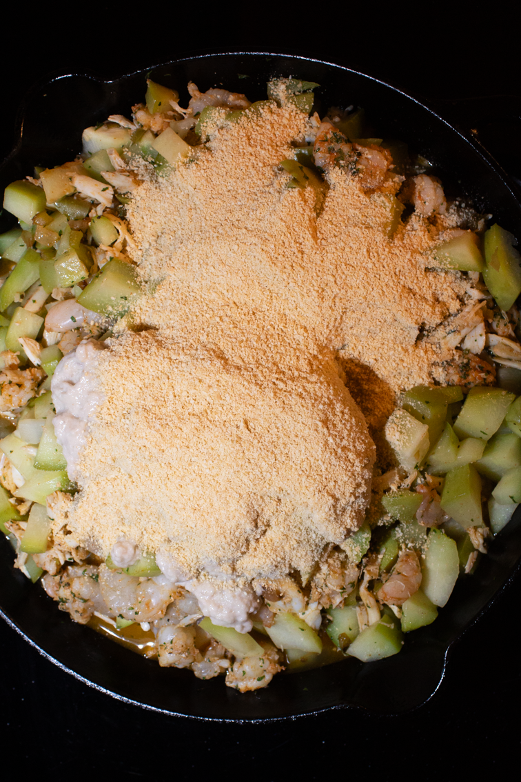 Cracker crumbs on top of mirliton dressing in a skillet. 
