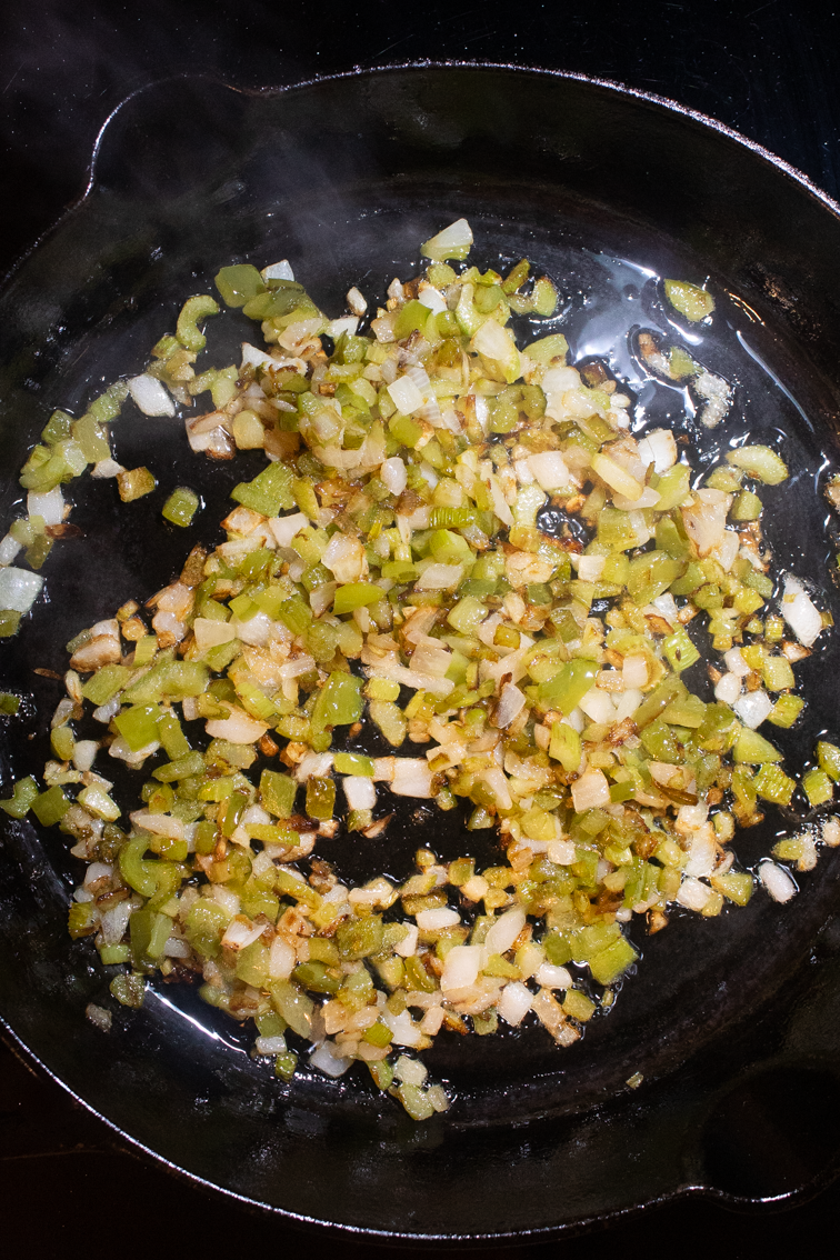 Browned chopped onion, bell pepper, and celery in a black pan. 