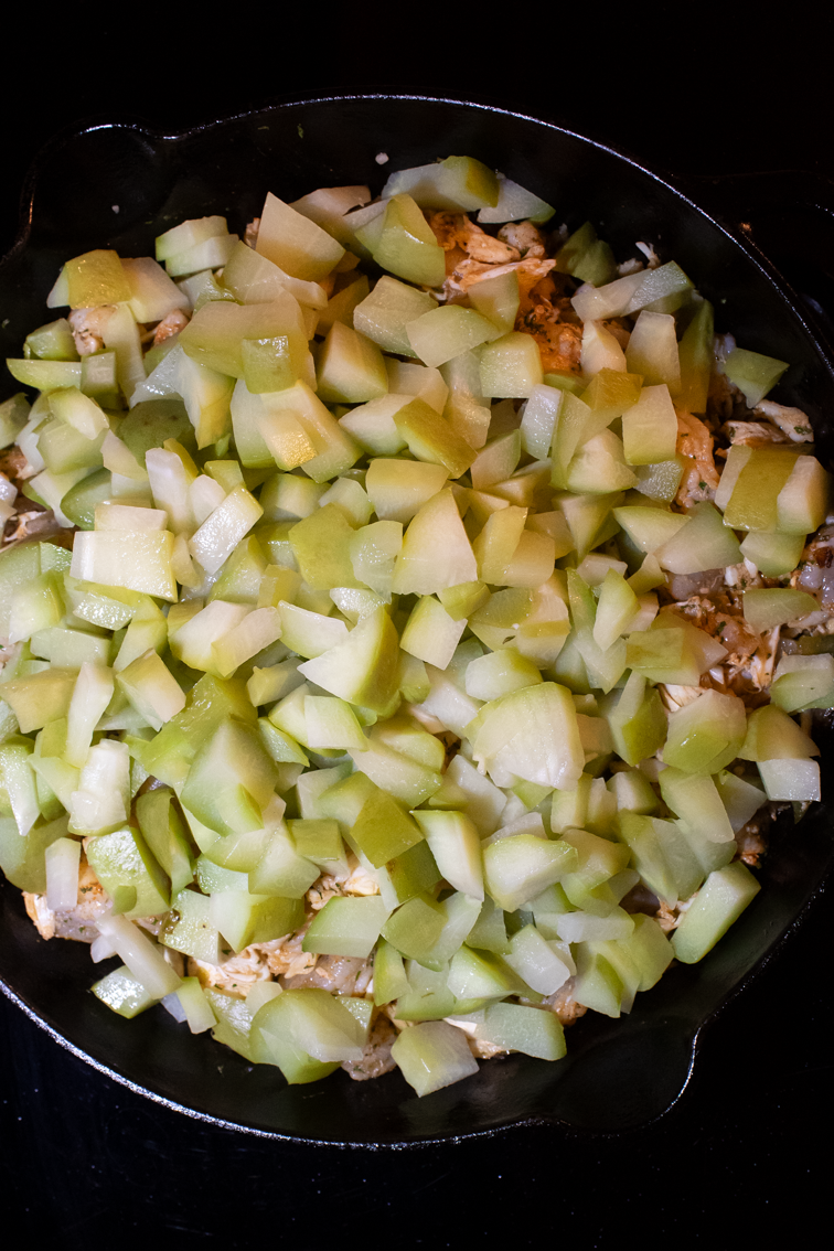 Chopped cooked mirliton squash on top of  vegetables and seafood in a pan. 