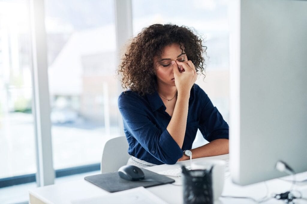 Woman at her desk rubbing her eyes, looking exhausted and overwhelmed, showing how a low winter mindset can affect mood and energy at work.