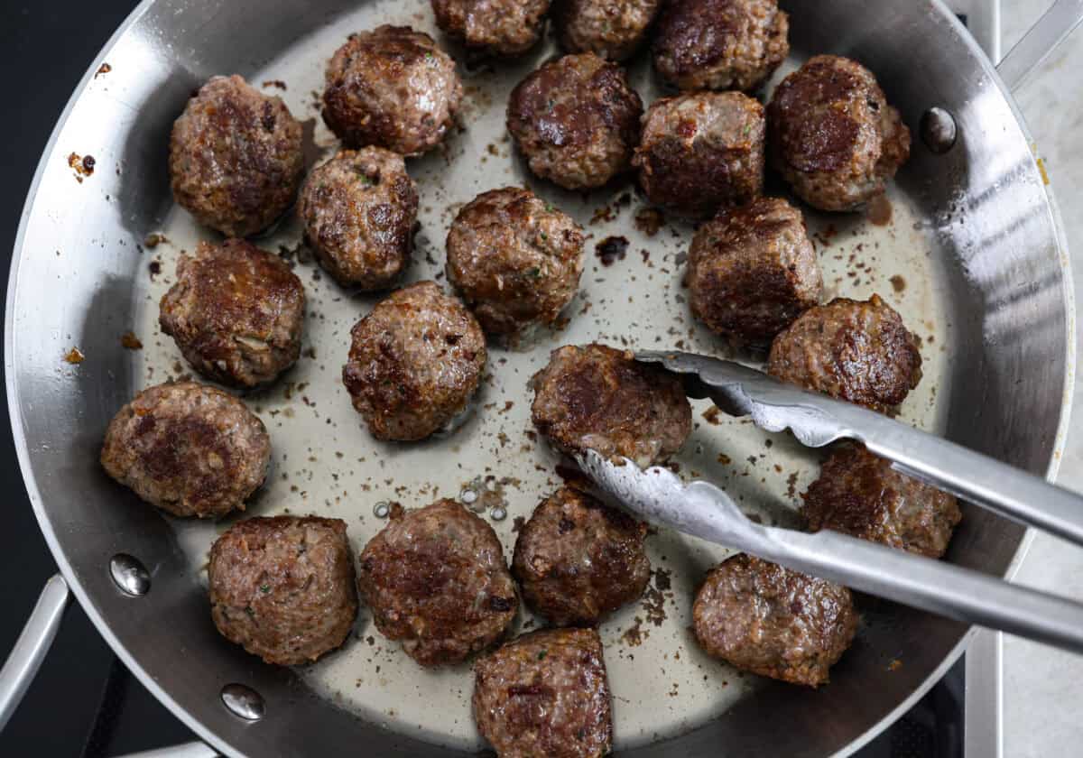 These Swedish Meatballs are smothered in the most amazing rich and creamy gravy and packed with such delicious flavor. You will quickly agree these are the BEST you have ever had! The top view of Swedish meatballs cooking in a pan.