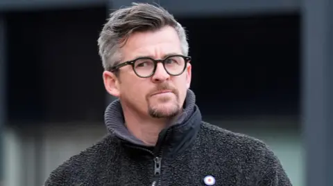 PA Media Joey Barton with grey hair and brown beard and black glasses wearing a grey hoodie.