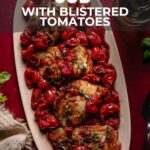 Oval platter with pan-seared cod fillets topped with blistered cherry tomatoes, set on a rustic table next to herbs, a fork, and a napkin. Text overlay provides recipe details.
