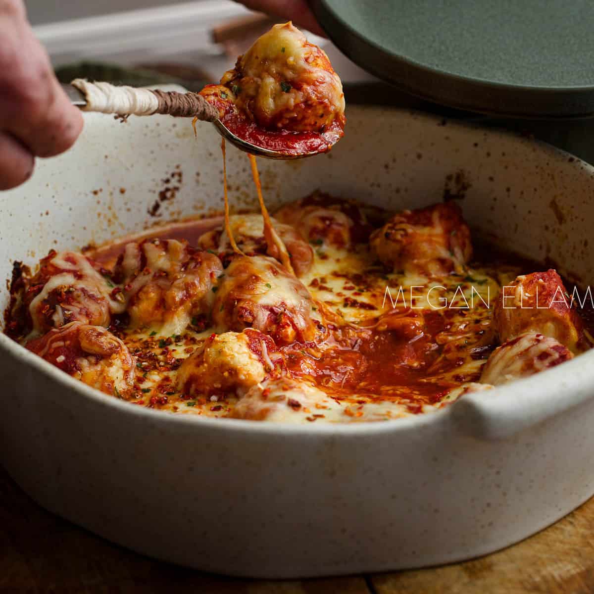 A close up of a man holding a spoon with a chicken meatball on it.