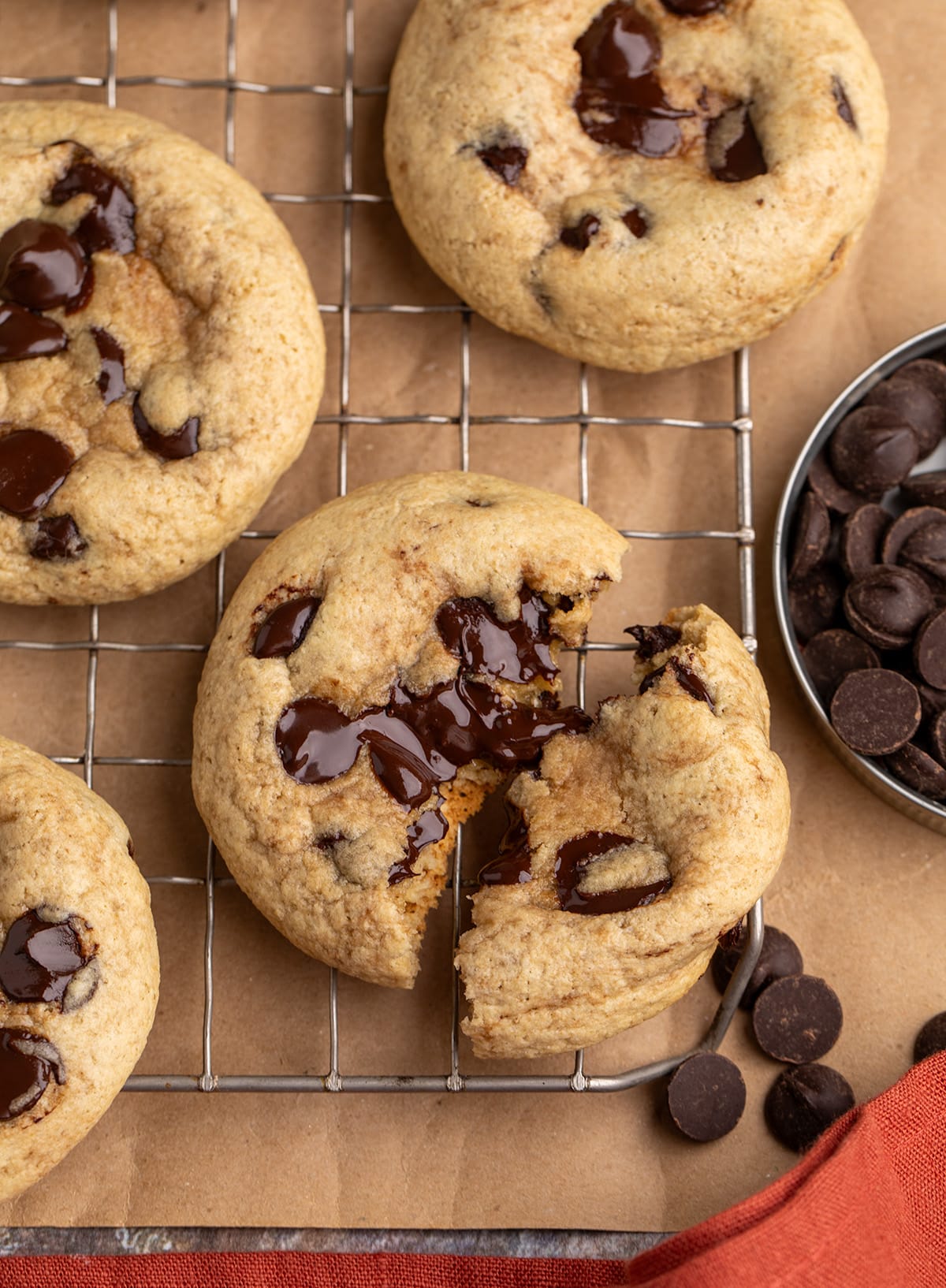 Chocolate chip cookies on a wire rack, with one cookie broken open and chocolate chips nearby.