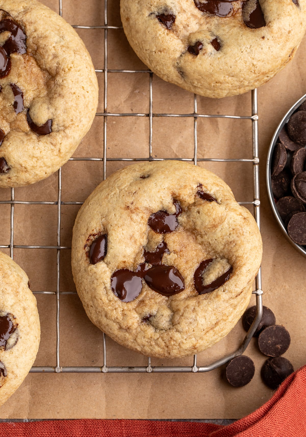Overhead image of chocolate chip cookies on a wire rack, with a bowl of chocolate chips nearby.