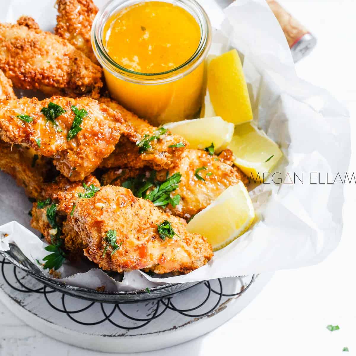 Crispy Lemon Chicken Wings on a white bowl with fresh lemon and herb butter over the top.