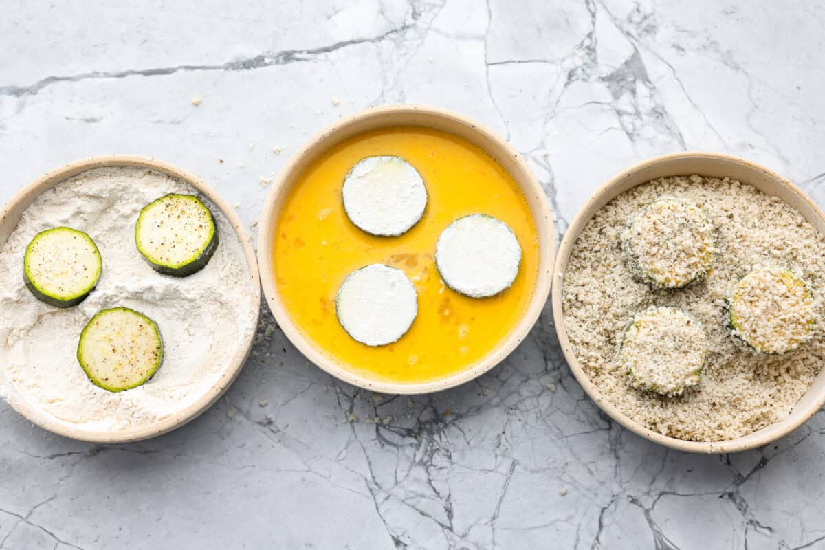 Zucchini slices in each of the dredging bowls.