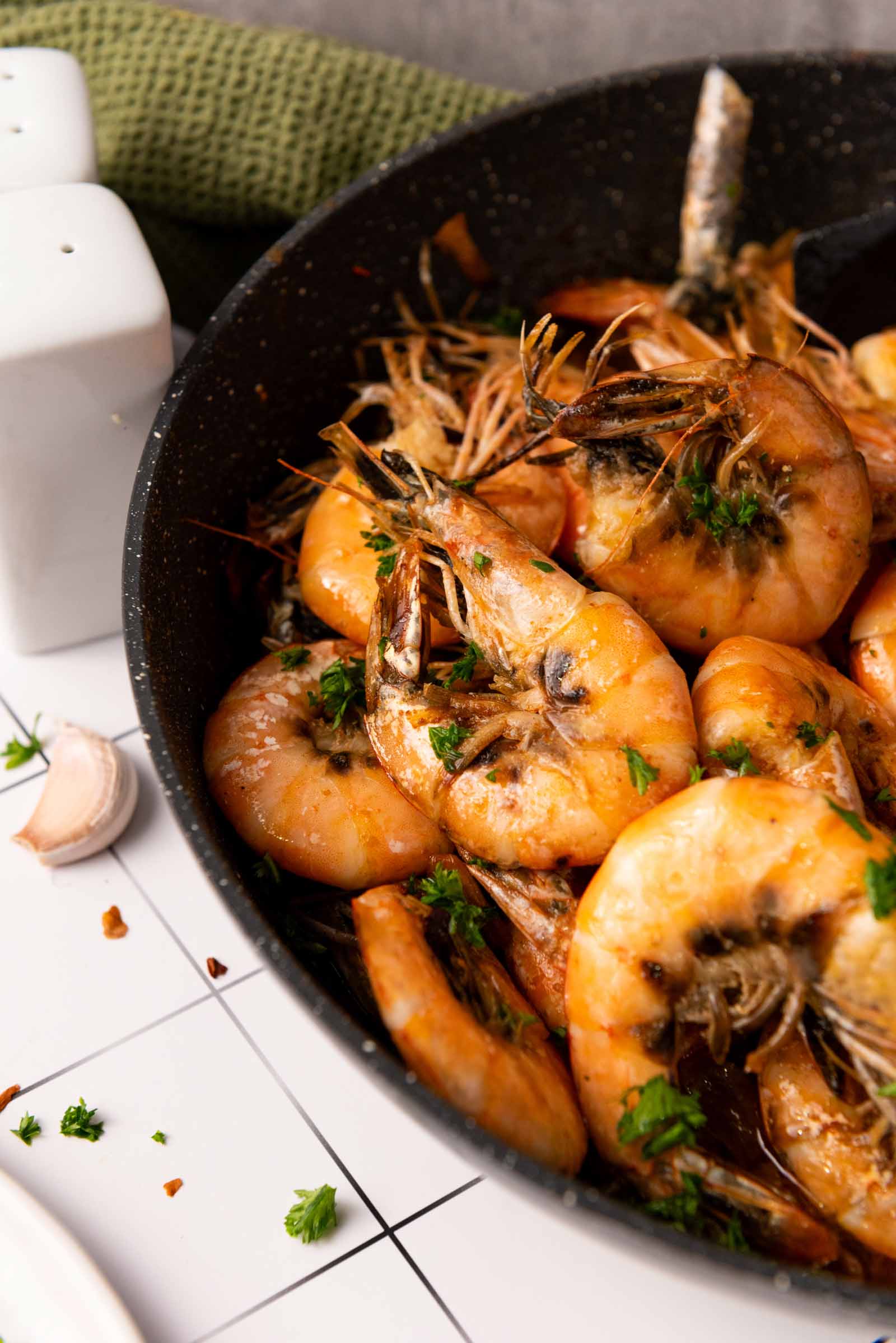 Cooked shrimp with herbs in a black pan, garnished with chopped parsley.