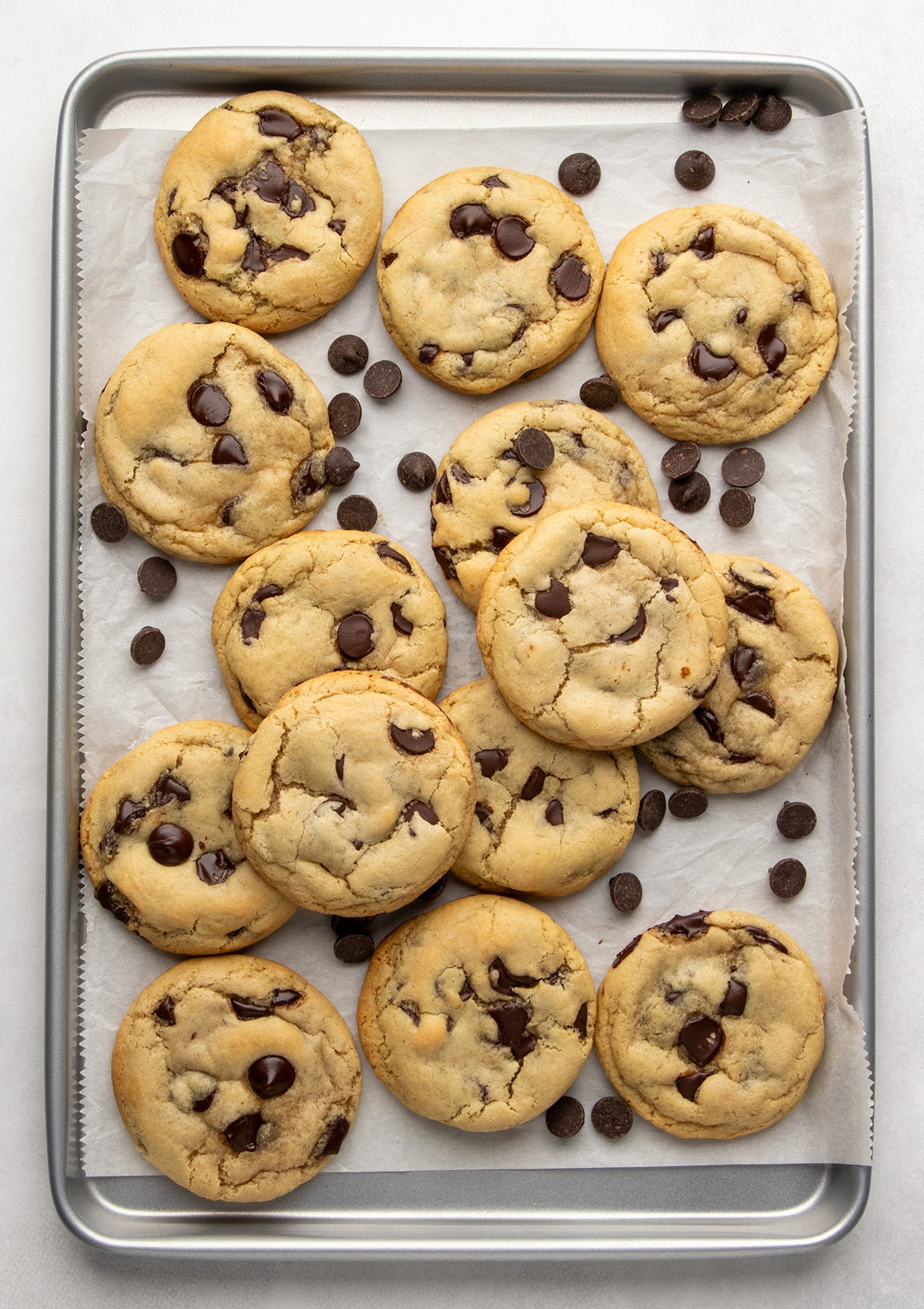 Baked chocolate chip cookies that are golden brown on the edges with loose chocolate chips on a parchment-lined baking sheet.
