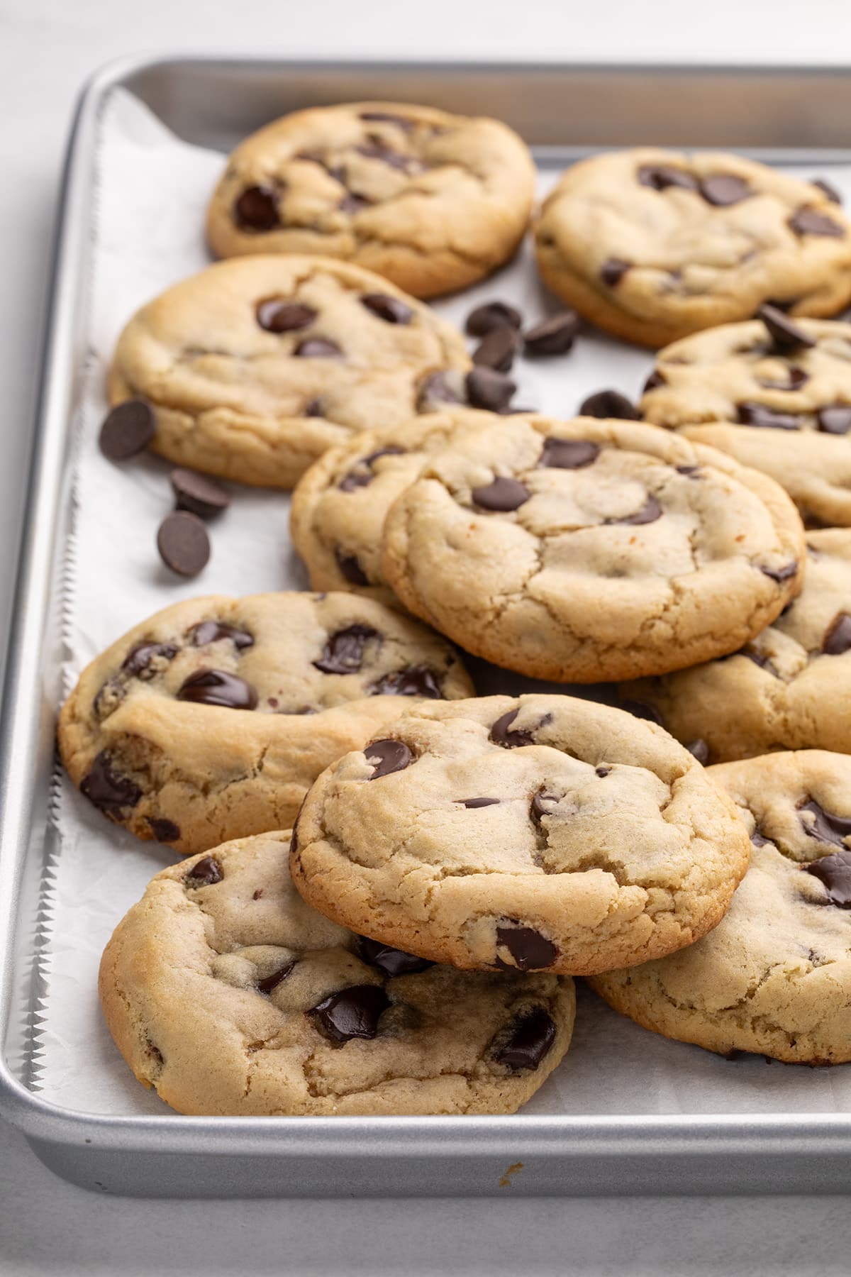 Side, backlit view of baked chocolate chip cookies stacked on a parchment-lined baking sheet.