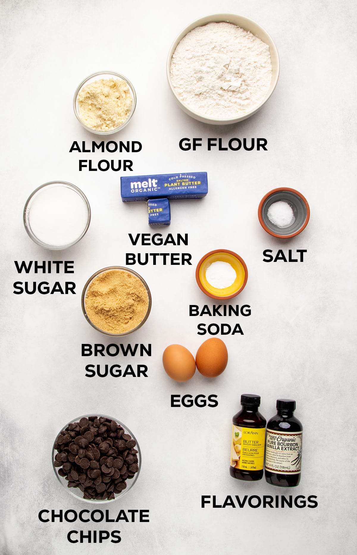 Labeled ingredients for chocolate chip cookies, including almond flour, gluten free flour blend, vegan butter, salt, white sugar, brown sugar, baking soda, eggs, chocolate chips, and flavorings.