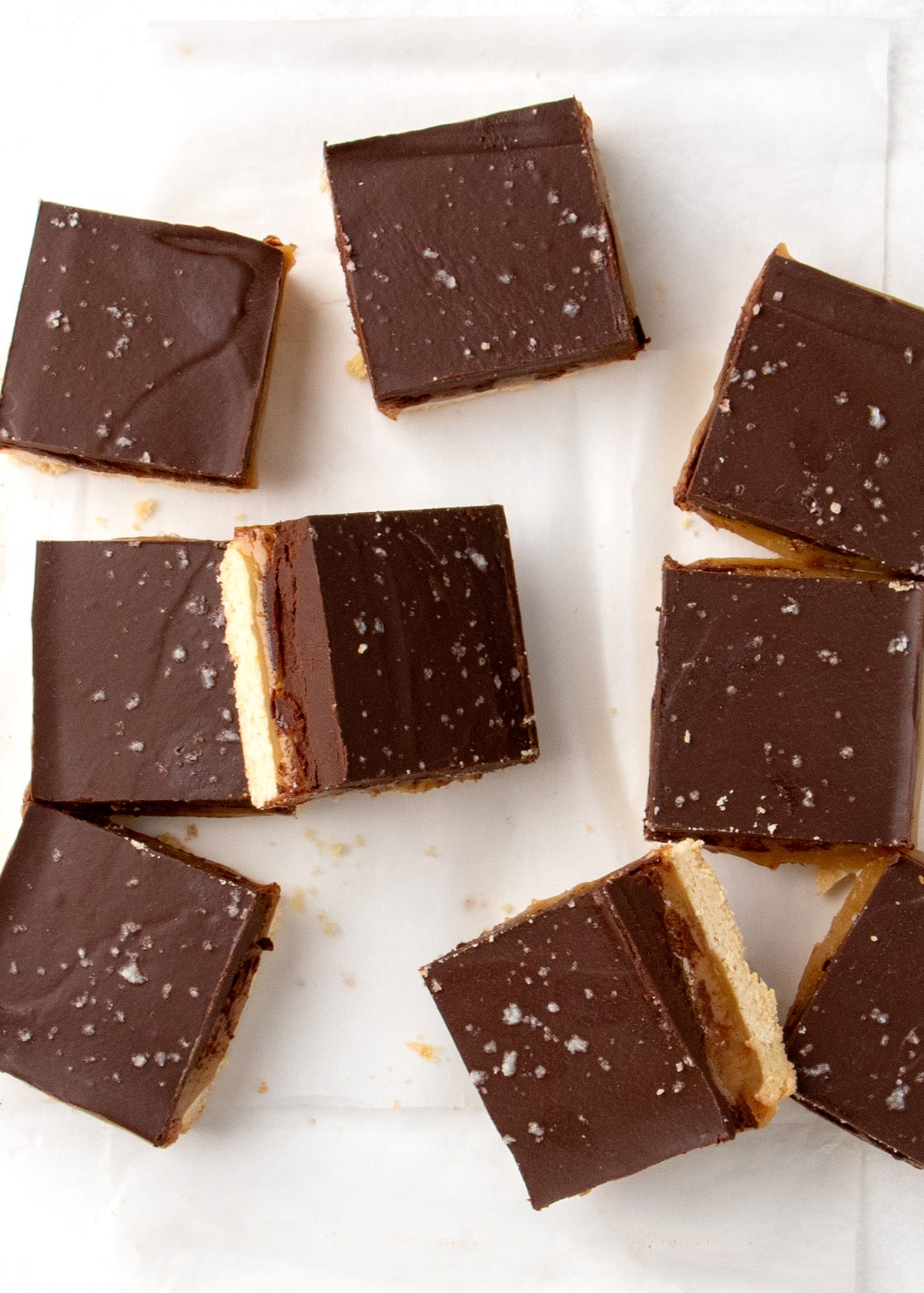 Chocolate-topped shortbread squares with coarse salt arranged on parchment paper.