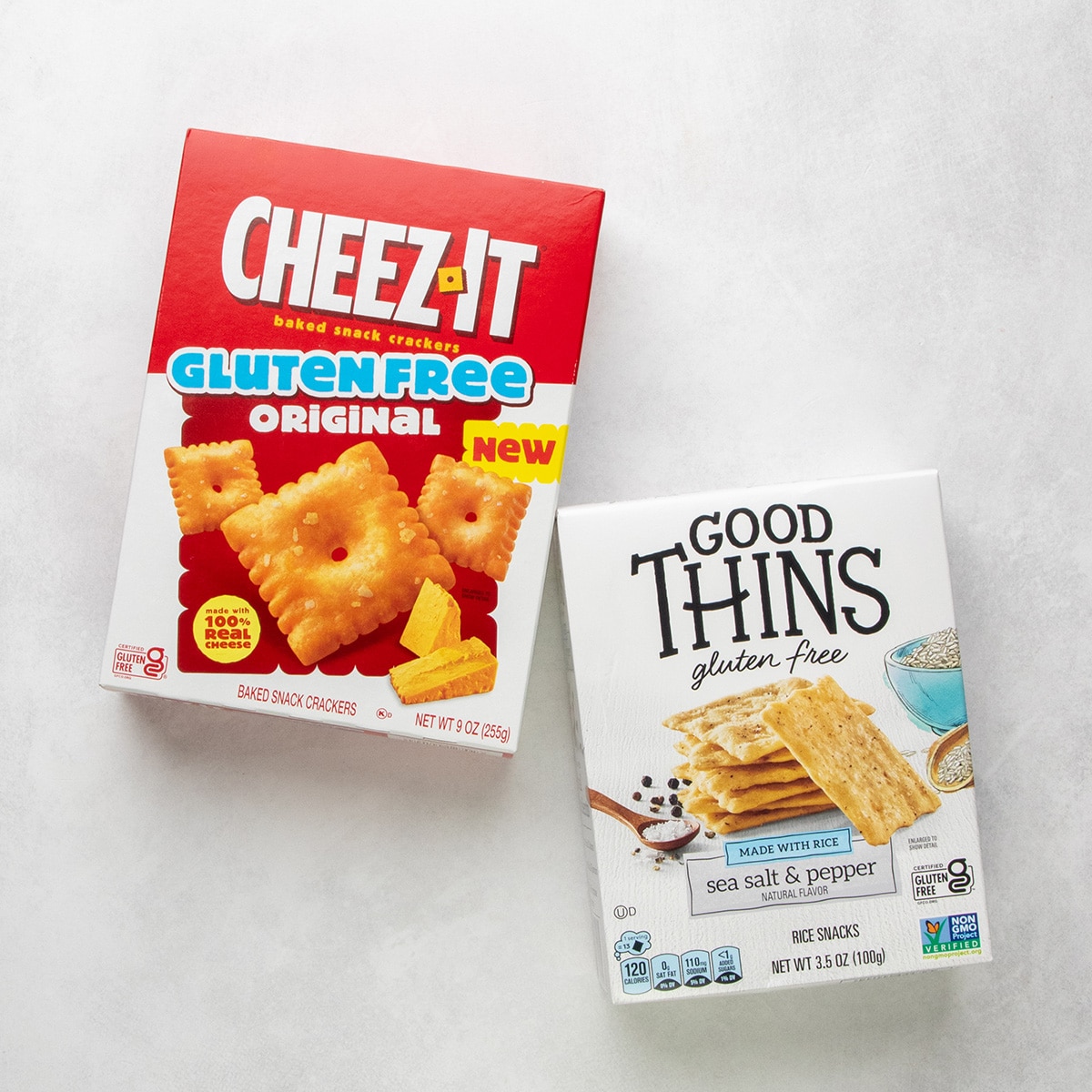 A box of Cheez-It gluten free original crackers next to a box of Good Thins gluten free sea salt and pepper rice snacks.