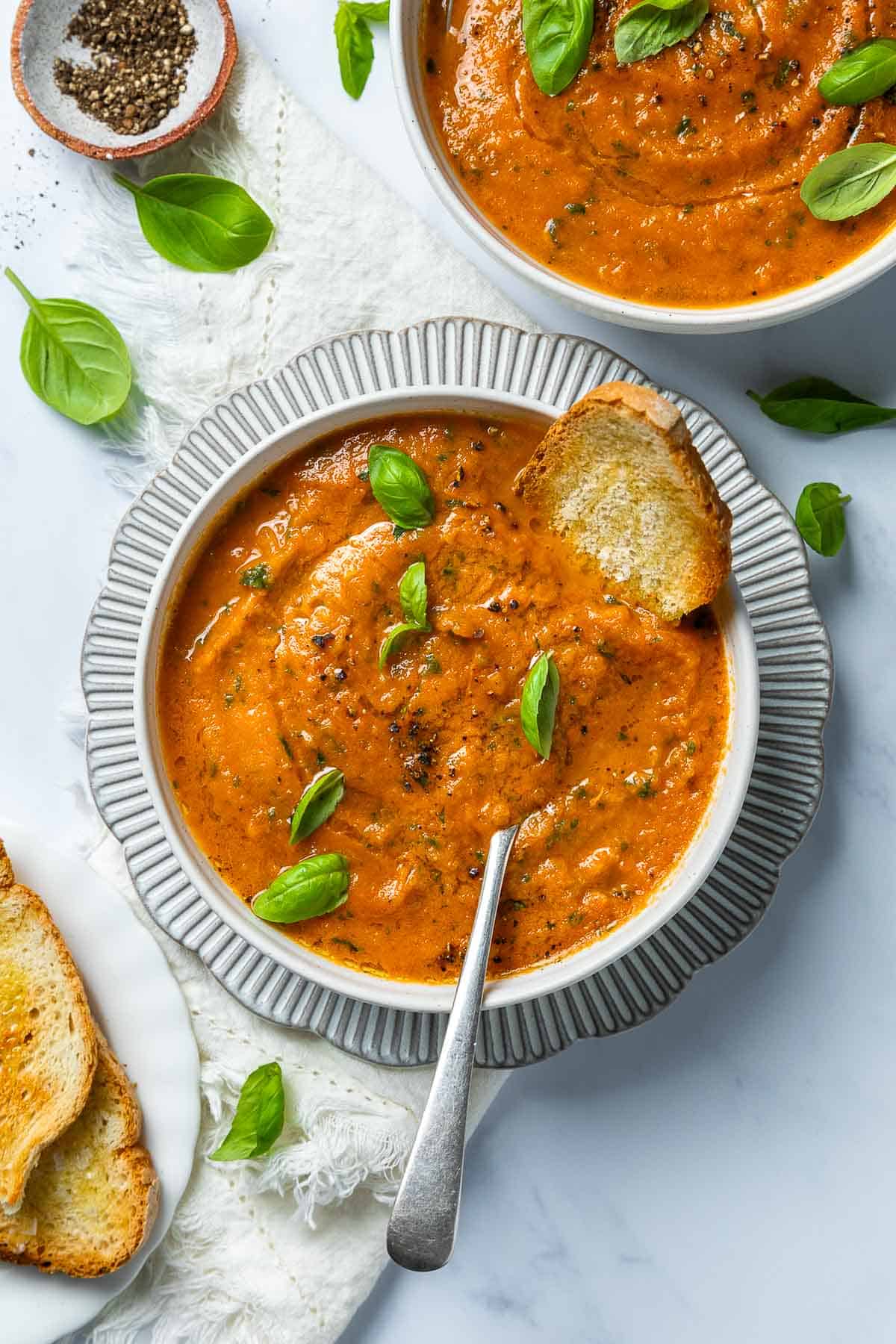 Roasted Tomato Garlic Soup in two bowls with a scattering of basil leaves.