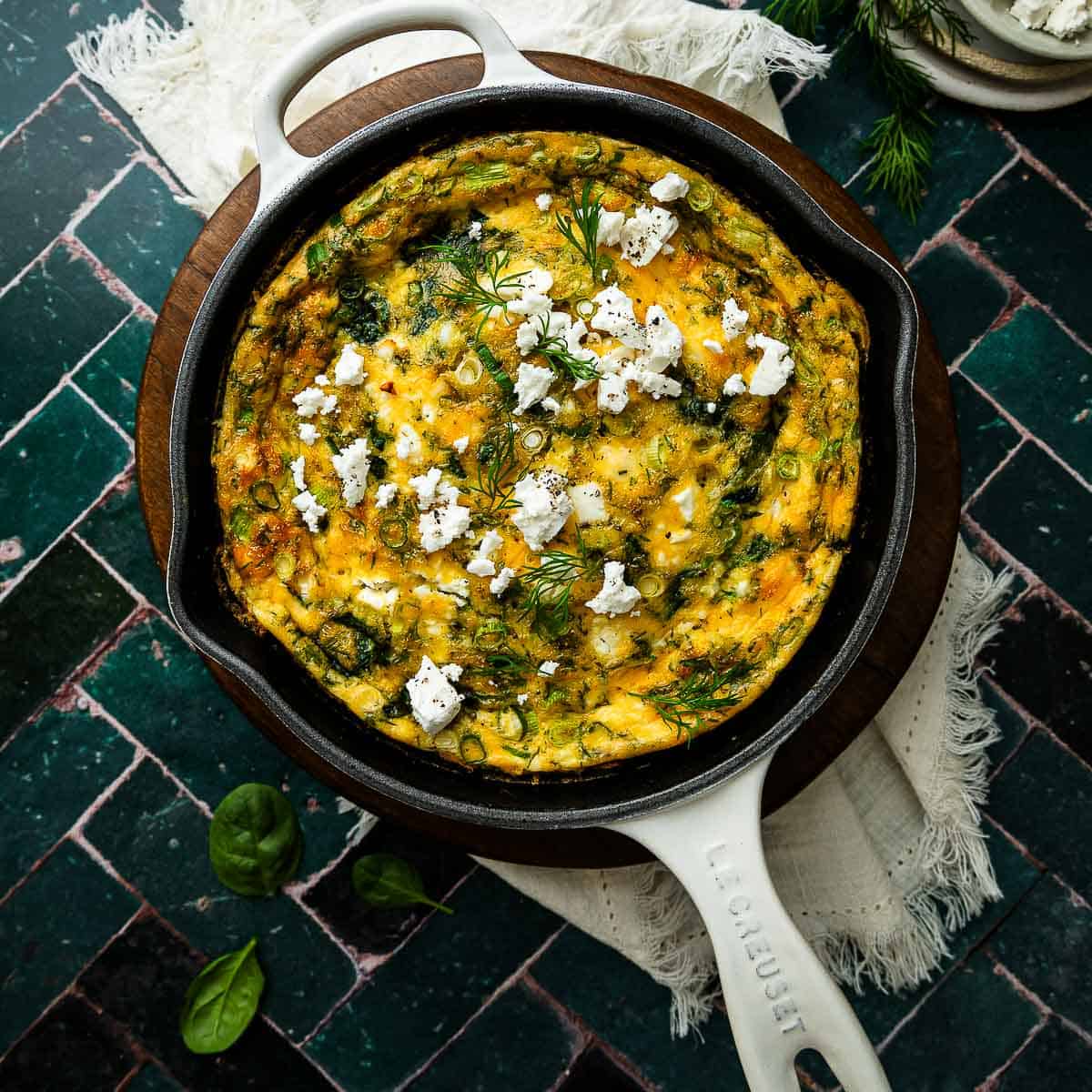 Spinach and Fetta Frittata in a cast iron pan on green tiles.