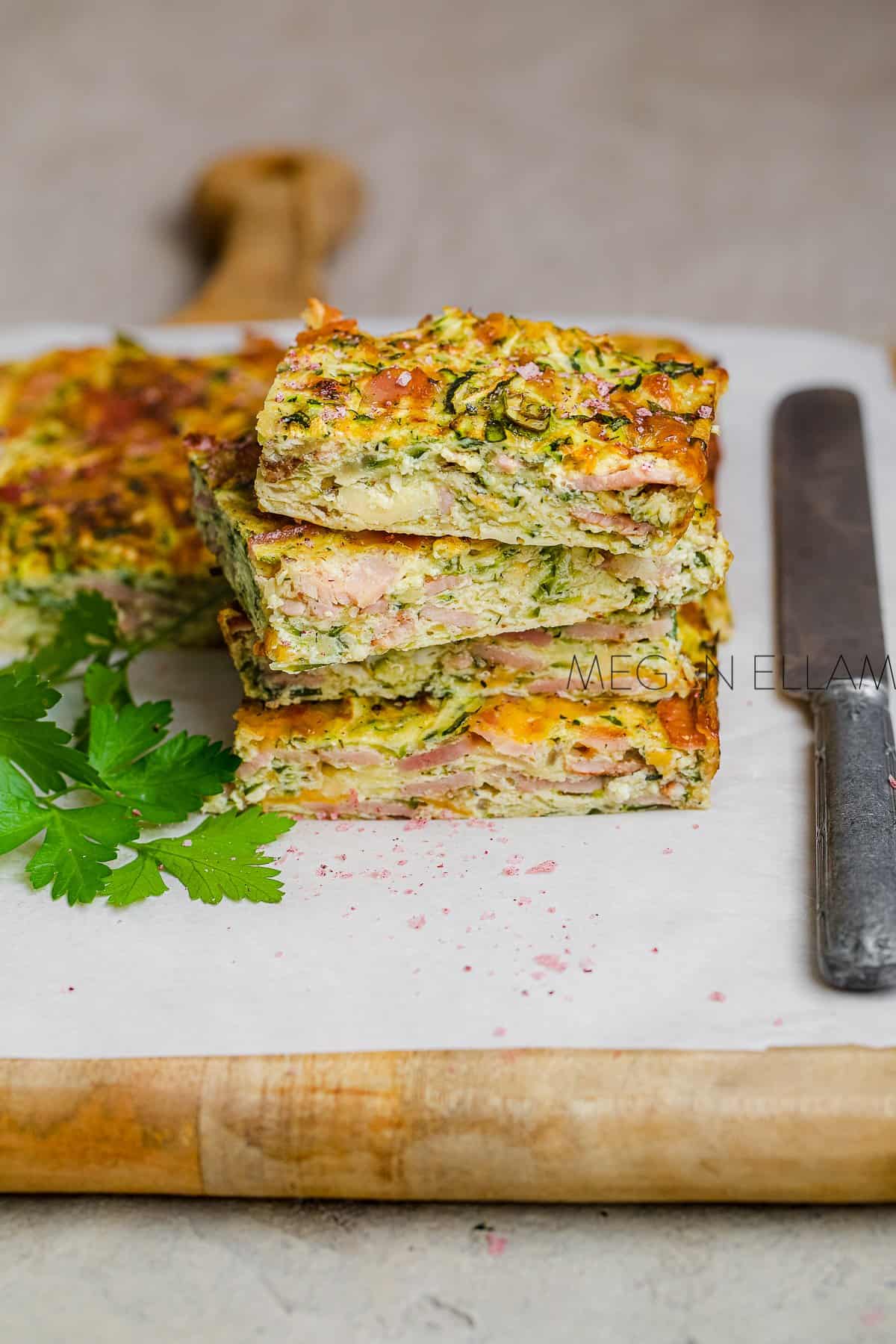 A stack of zucchini quiche slices on a piece of baking paper.