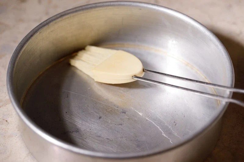 Metal baking pan being greased with oil with a silicon brush.