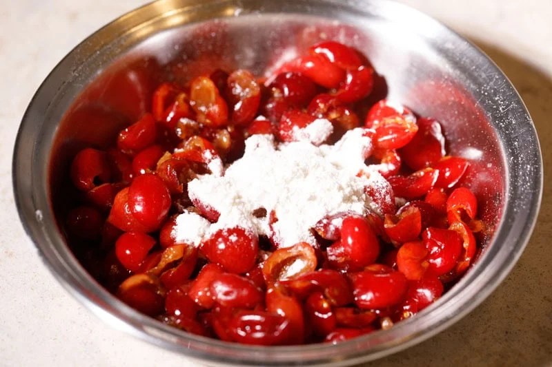 Some flour on top of chopped red cherries in a bowl.