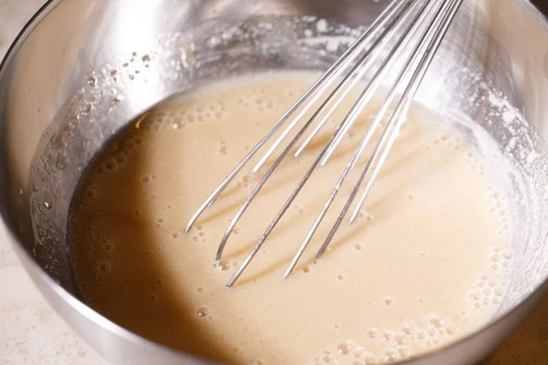 Wired whisk mixing sugar with buttermilk in bowl.
