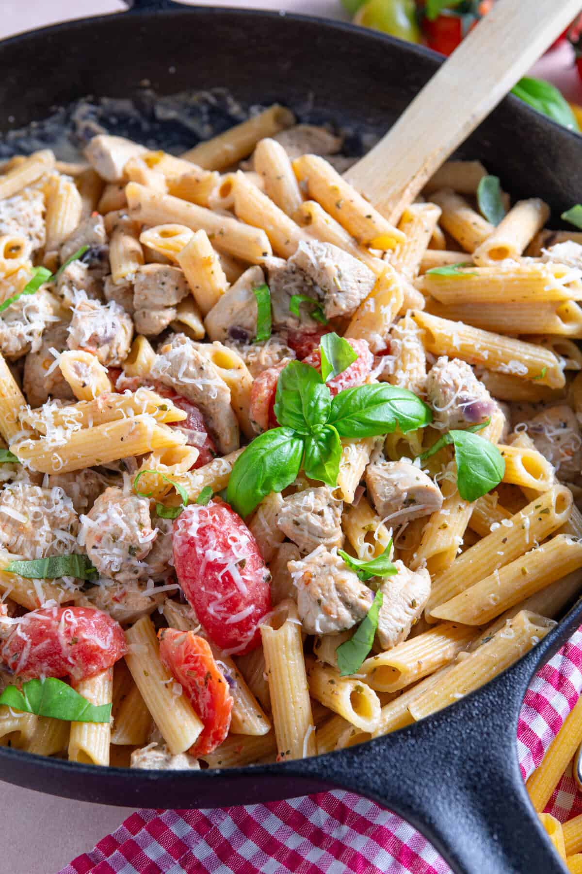 Close up of a pan of creamy chicken and tomato pasta with parmesan and basil on top.