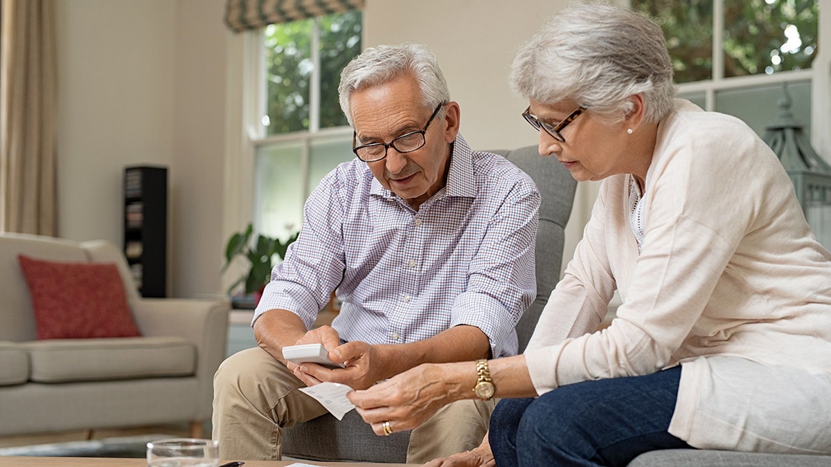 An elderly couple sits together calculating a receipt.