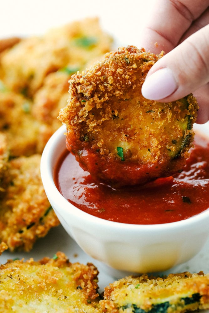 Dipping a fried zucchini slice in marinara sauce.