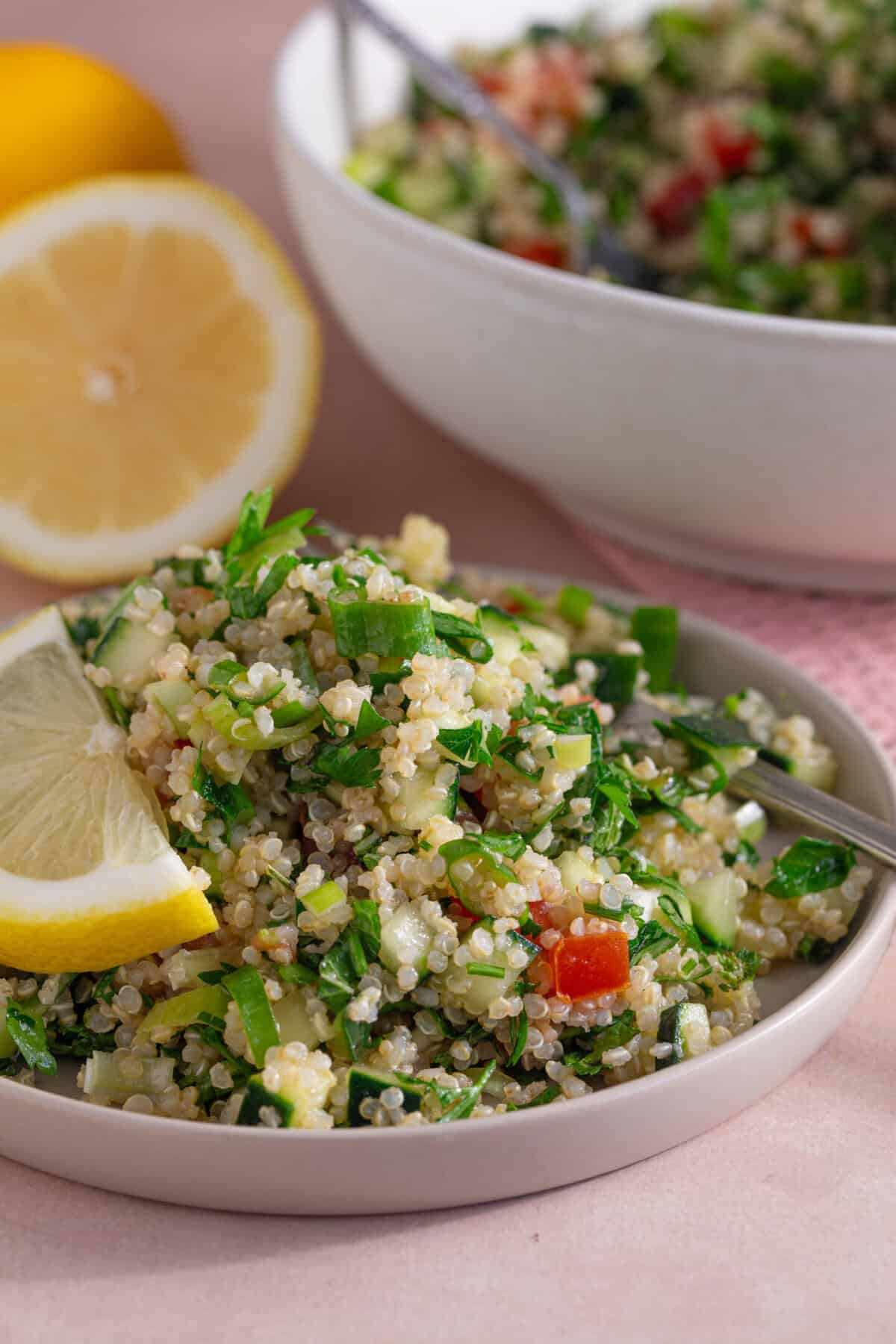 A serving bowl of gluten free tabbouleh with a lemon and the main bowl of salad behind.