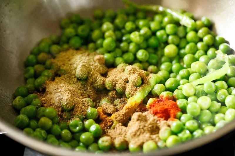 Ground spices on green peas or matar in pan.