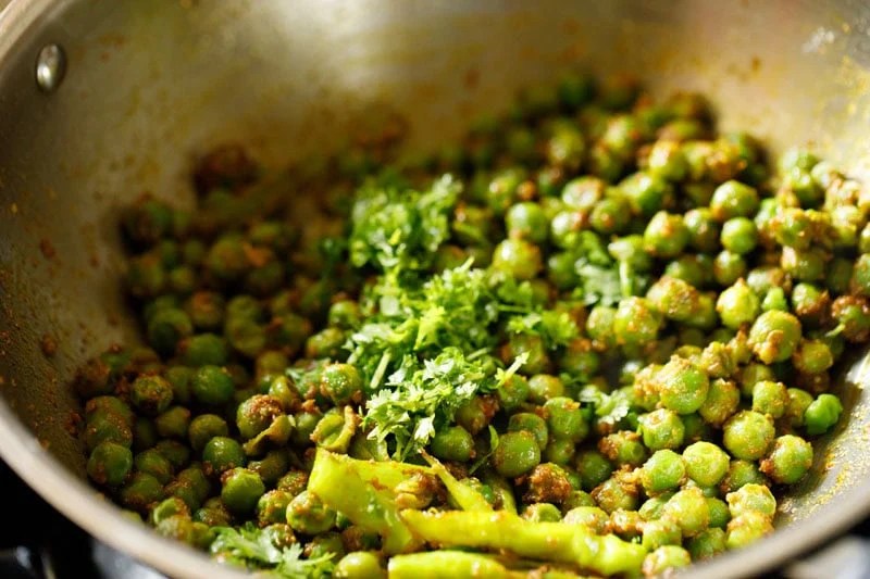 Chopped coriander leaves on dry green peas sabji in pan.