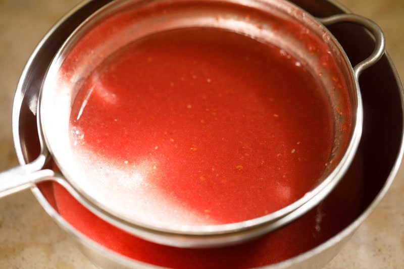 Straining red raspberry juice in a bowl.