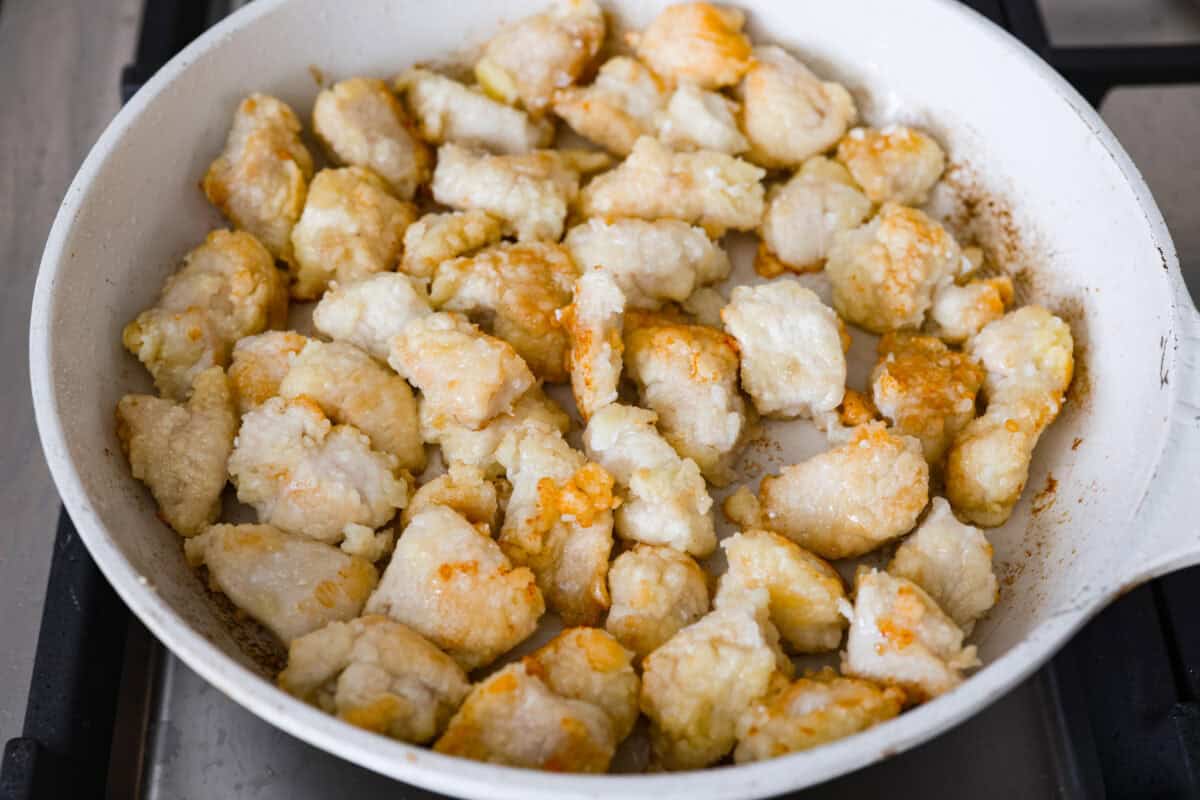 Coated chicken pieces cooking in a skillet.