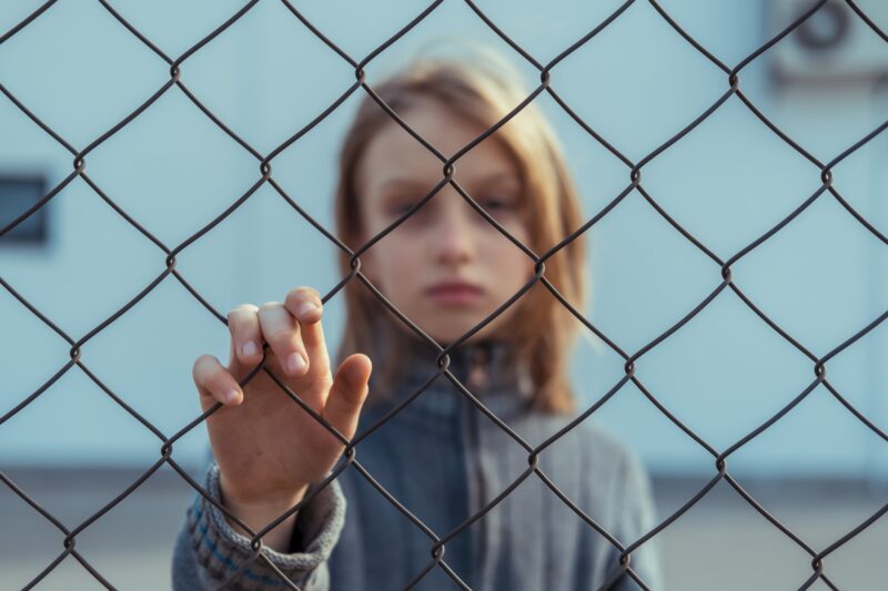 Sad girl standing behind a wire fence