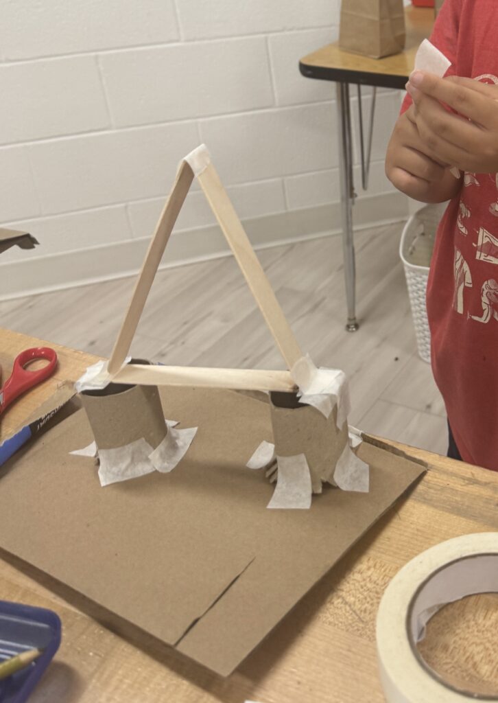 an image of a student using recyclable materials to construct a strong bridge