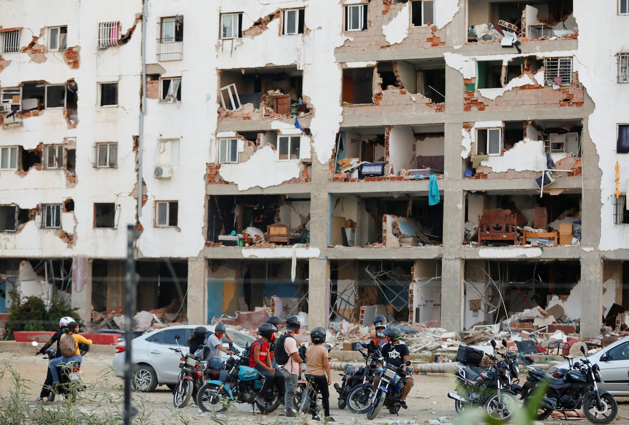 People in motorcycle helmets look at the remains of a building.