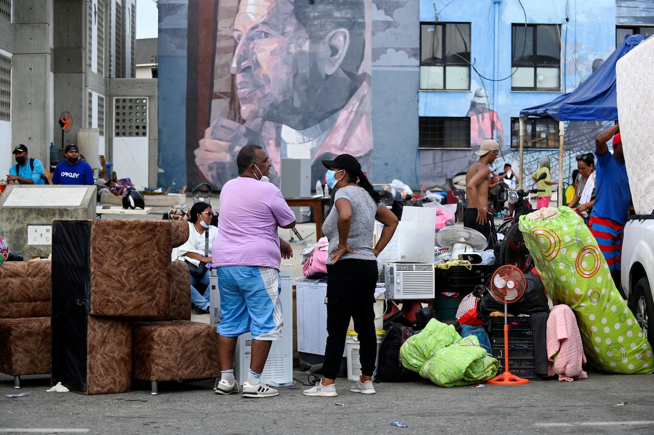 People stand with their belongings outside.
