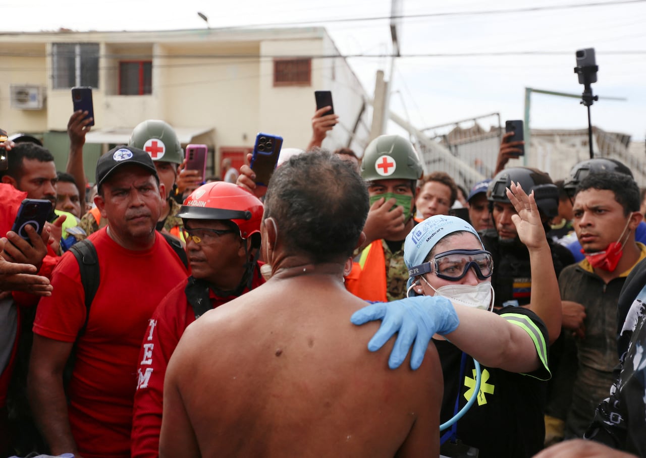 A nurse places her hand on a man's back, as a crowd gathers behind her.